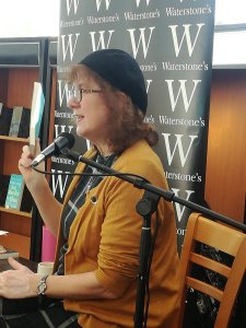 Profile photo of Debbie at microphone with Waterstones banner behind
