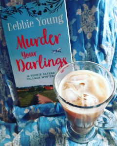 image of a glass of iced coffee with a copy of Murder Your Darlings against a blue cotton sarong